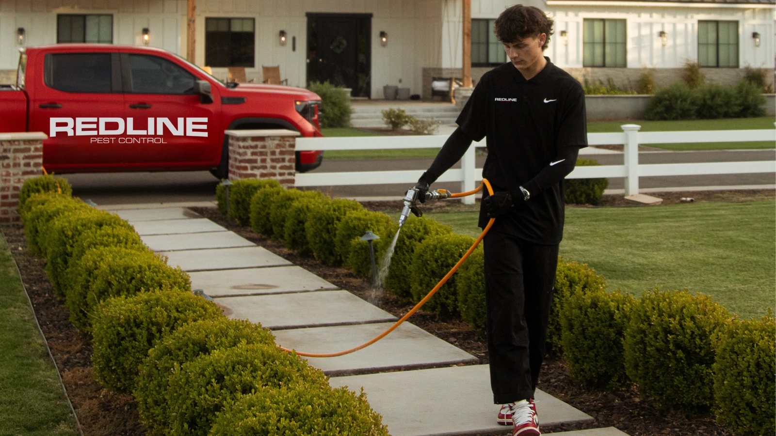 Davin Allen, owner of Redline Pest Control, treating the walkway of a home with the Redline truck parked behind him